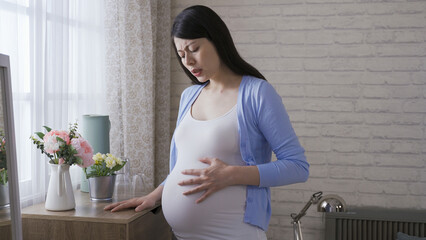 asian woman in the last trimester is feeling sudden pain in the abdomen in the morning by the...