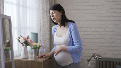 waist up japanese expectant mother propping herself on the cabinet is suffering labor contraction...