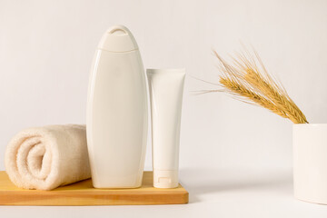 A bottle of shampoo and cream, a white towel, a white mug with ears of wheat.