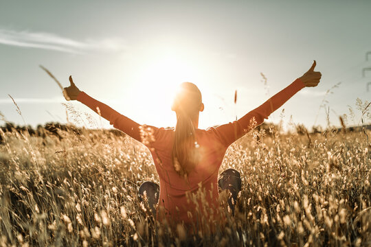 Having a positive mindset, wellbeing and hope concept. Happy young woman in a nature sunrise field with arms outstretched.	thumbs up