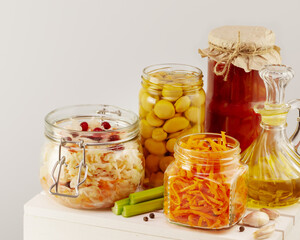 Autumn seasonal pickled or fermented vegetables, mushrooms and olive oil in glass jars on a white wooden board on a light neutral background. Fall home food preserving or canning