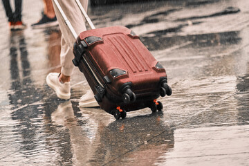 Suitcase close-up carries a girl on a wet road. A lonely man walks on a wet pavement in the rain...