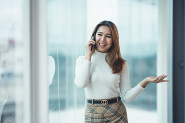 Fototapeta premium Smiling Asian businesswoman enjoying the phone, answering questions, talking to customers on the phone and comment in the office.