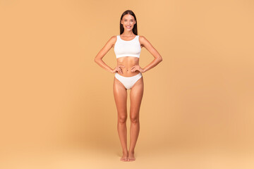 Slim woman in white underwear with perfect body shape and flat tummy posing over beige studio...
