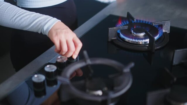 Female hand turns on kitchen cooktop gas burner and natural gas ignites burns with blue flame. Human hand lighting gas stove burner. Household faces rise in gas prices