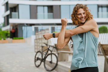 Fototapeta na wymiar Young athletic long-haired handsome smiling man stretching his shoulder