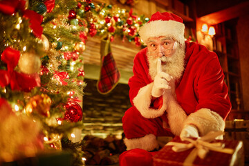 Fototapeta na wymiar Portrait of traditional Santa Claus putting presents under Christmas tree in secret