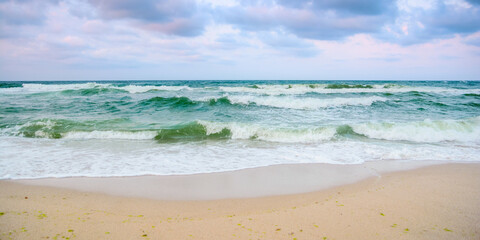 sandy beach before the storm. evening scenery with heavy clouds in colorful light. turquoise waves rushing on the shore. windy weather