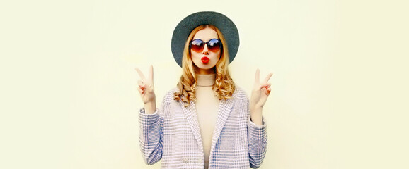 Portrait of stylish woman model blowing her red lips sending air kiss wearing round hat, jacket on white background