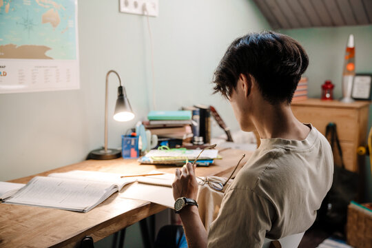 Serious asian guy studying with book while sitting at desk at home