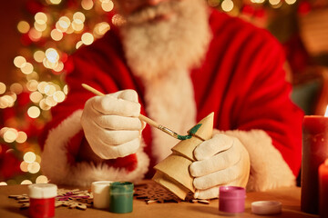 Close up of traditional Santa Claus painting wooden toys in workshop on Christmas eve, copy space