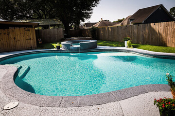 A large free form gray grey accent swimming pool with turquoise blue water in a fenced in backyard...