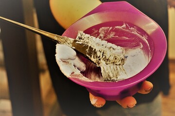 Pinke Plastikschüssel mit Haarfärbemittel und schwarzem Pinselkamm in Hand von Frisörin in Salon 