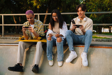 Three young smiling happy friends with phones sitting together.
