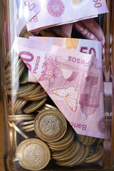 Muchos billetes de 50 pesos y monedas están en la alcancía de cristal.

