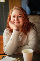 Close-up portrait of a young beautiful red-haired plump girl in a cafe.