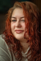 Naklejka premium Close-up portrait of a young beautiful red-haired plump girl in a cafe.