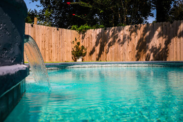 Close up of a gray grey accent swimming pool with turquoise blue water in a fenced in backyard in a suburb neighborhood