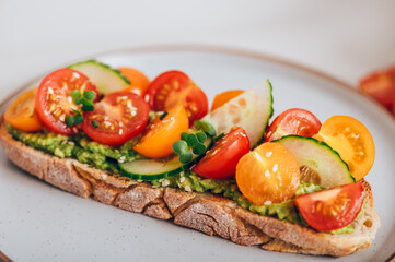 Tasty open sandwich from toasted sourdough bread with mashed avocado and fresh tomatoes