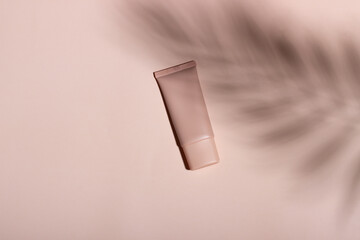 Cosmetic cream or mask in a white tube with hard shadows from the leaves on a white background. Natural organic care for face and body skin. View from above.