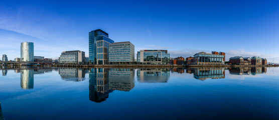 panorama skyline of downtown Belfast with skyscrapers and reflections in the calm River Lagan at dawn - obrazy, fototapety, plakaty