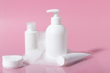 Cosmetics for face, body and hair care. Moisturizer, shampoo or facial cleanser on pink background with foam