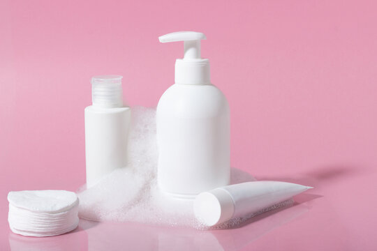 Cosmetics for face, body and hair care. Moisturizer, shampoo or facial cleanser on pink background with foam