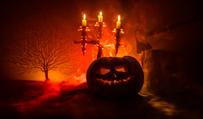 Scary orange pumpkin with carved eyes and a smile with burning candles and an ax