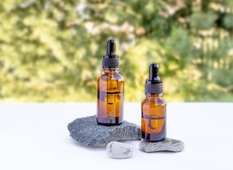 Two brown bottles of essential oil, essence, serum for women's skin care on a natural background. Stone podium. Front view