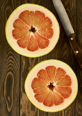 Cut ripe red pomelo fruit on a wooden table, top view