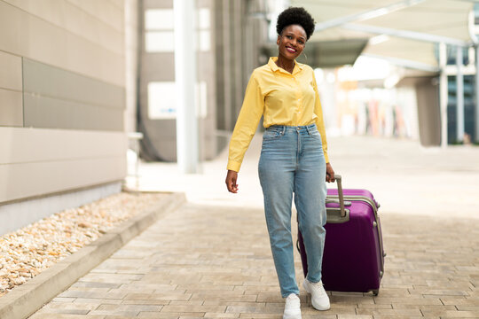 Joyful Black Female Posing With Suitcase Walking At Airport Outdoors