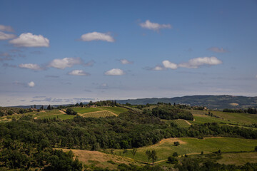 Fototapeta na wymiar Rural view of Tuscany with rolling green hills and traditional Tuscan architecture on a partly sunny day.