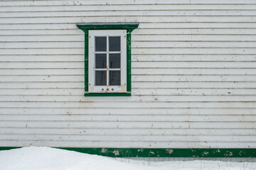 The exterior outside wall of a stark white heritage wooden building with a single window. The...
