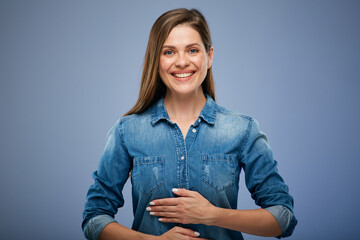 Smiling happy woman in blue shirt holding hands on stomach. isolated portrait on blue studio...