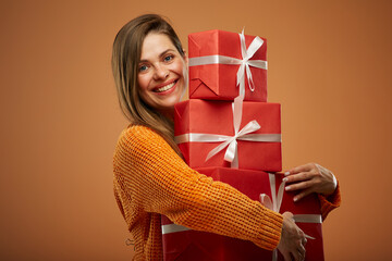 Happy woman holding stack of gift boxes. Isolated female portrait in christmas style on orange background. - 532024343
