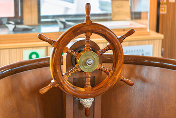 Close-up of a fake varnished wooden ship's wheel called a helm steered by a helmsman tied with a sailor's coil knot and used to change the rudder's angle so that the pirate's ship can turn on the sea. - obrazy, fototapety, plakaty