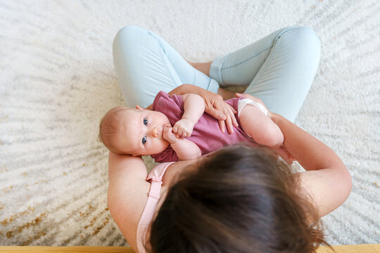 Portrait of a cute chubby baby lying on the lap of a young mother sitting on the carpet on the floor