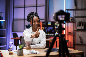 Smiling successful african american skilled businesswoman in formal wear recording new video for her internet business course and showing thumb up.