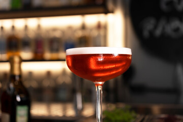 A glass of red alcohol drink with foam and flower petal. Cocktail garnish. Close-up. Selective focus.