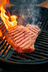 Barbecue dry aged wagyu porterhouse beef steak grilled as close-up on a charcoal grill with fire and smoke