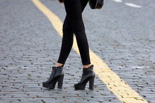 Crossed Female Legs In Black Tight Jeans And Boots On High Heels. Slim Girl Standing On A Road, Fashion In Autumn City, Hitchhike Travel