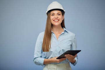 Smiling woman engineer in safety white helmet using digital tablet. Isolated female portrait on blue background.