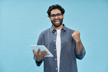Happy young arab man student winner winning online raising fist in yes gesture using digital tablet...