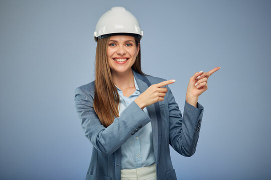 Smiling woman builder engineer in safety industrial helmet pointing with fingers. Isolated female portrait.