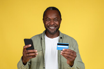 Glad middle aged african american guy shopaholic in casual with credit card and smartphone