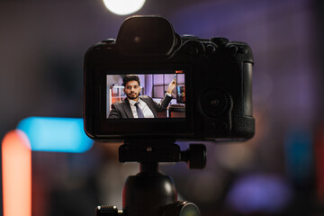 Focus on camera screen. Attractive confident arab skilled bearded businessman explaining online economic charts on glass board to his colleagues sitting in front of video camera.