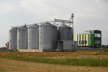 Fototapeta na wymiar Modern grain dryer and farm granary buildings on harvested field background . Beautiful countryside industrial landscape