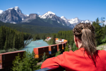 Fototapeta na wymiar Woman watches a freight train pass by on the Morant's Curve viewpoint on the Bow Valley Parkway in Banff National Park Canada