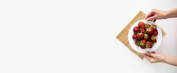 Female hands hold a plate with strawberries on a white table background. Top view, flat lay. Banner
