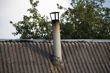 Old chimney pipe on rural weathered house roof on green tree background . Warming in countryside
